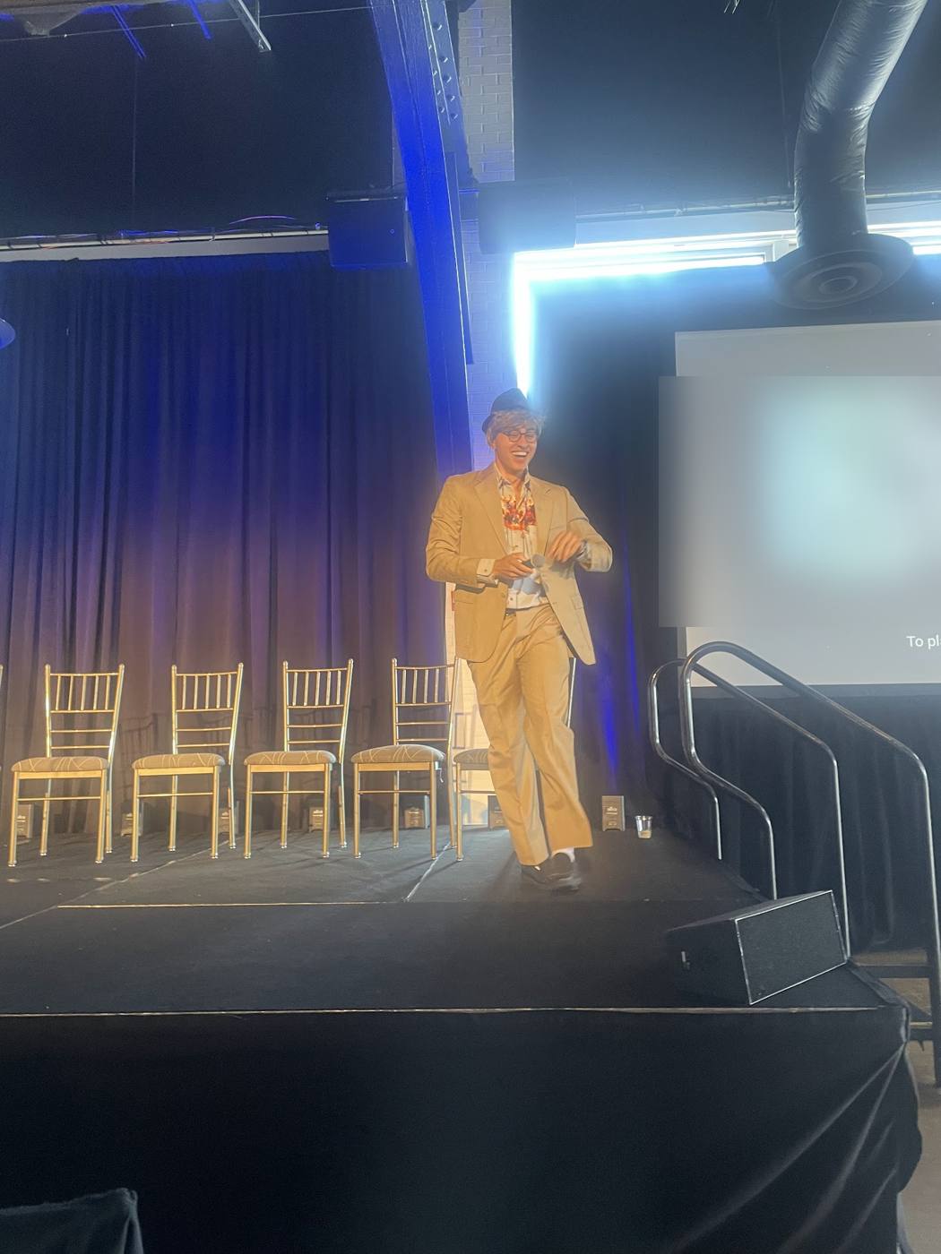 Cesar in a tan suit and hat hosting trivia on stage